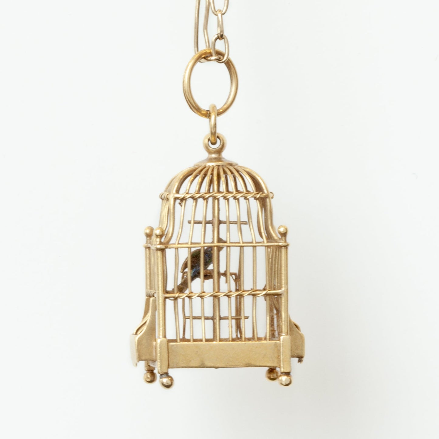 A gold birdcage pendant charm with a small bird inside, suspended from a matching gold chain against a plain white background.